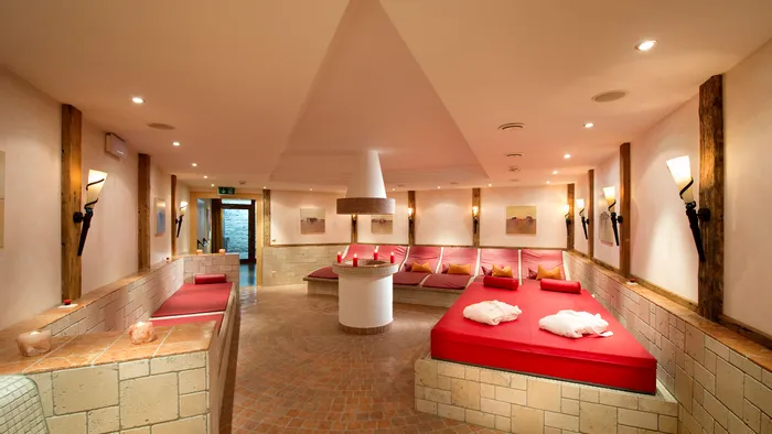 Sala relax benessere con lettini rossi, illuminazione soffusa e pareti in pietra naturale